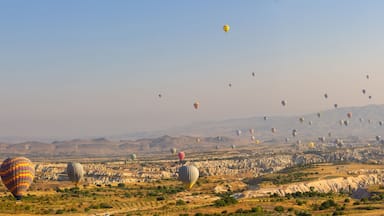 A landscape with numerous hot air balloons in the sky and a rocky terrain below.