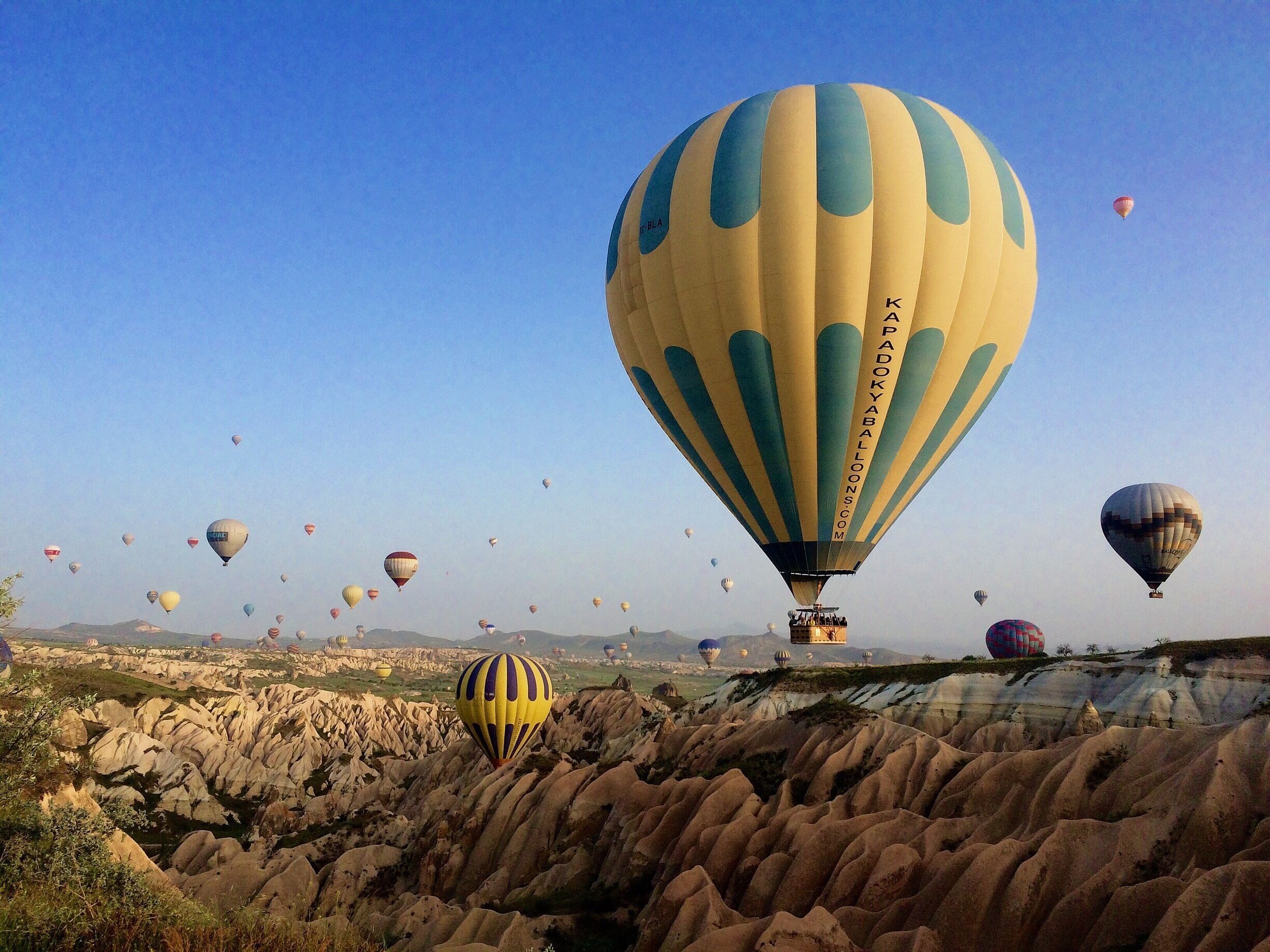 A landscape with numerous hot air balloons in the sky and a rocky terrain below.