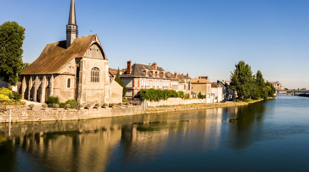 A historic church with a tall steeple, a calm river, and traditional buildings along the riverbank.