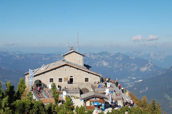 Ein Berggasthof mit Steingebäude, einer Flagge und Blick auf schneebedeckte Berge.