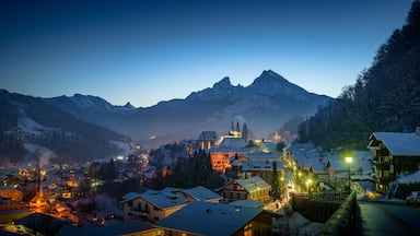 A snow-covered village with illuminated buildings, a church, and mountains in the background.
