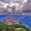 A mountain lodge with a steep staircase, surrounded by pine trees and overlooking a valley.