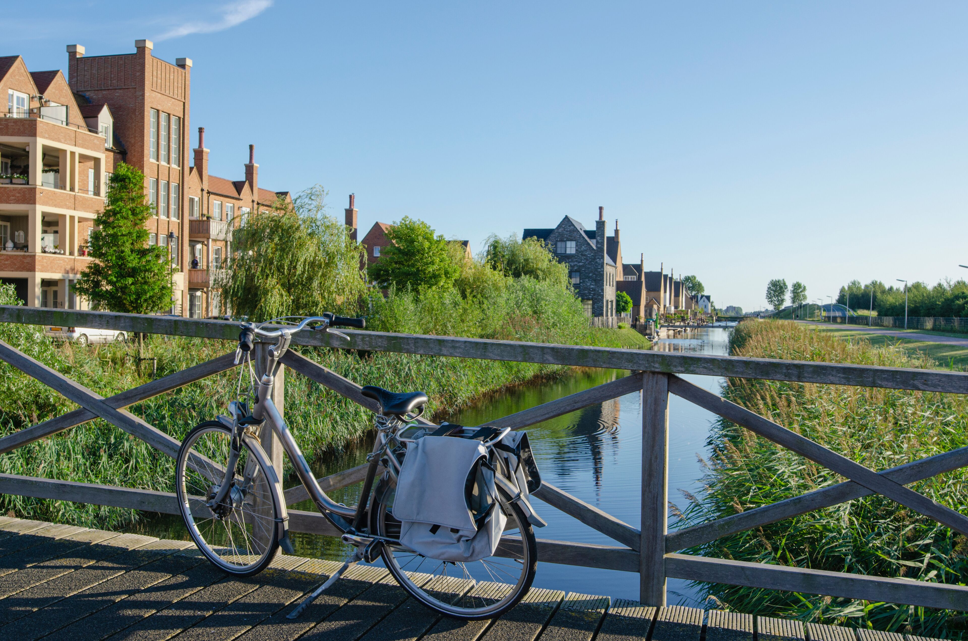 Canal view from bridge in Hoofddorp, the Netherlands. With a bicycle in the foreground. A few new-built buildings, a lot of greens.