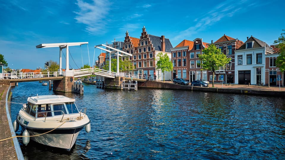 A canal with a boat docked, a pedestrian bridge, and historic buildings along the water.