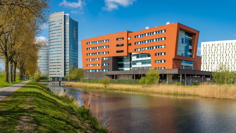 Un complesso di edifici moderni con un fiume in primo piano e alti grattacieli sullo sfondo.