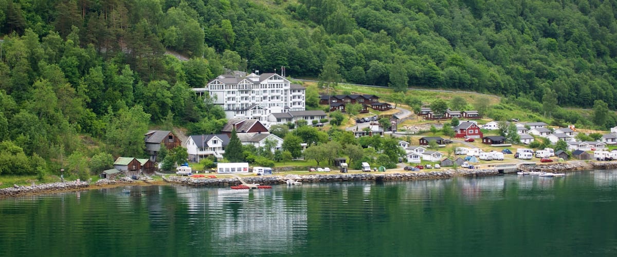 A lakeside village with a prominent white building surrounded by smaller houses and boats.