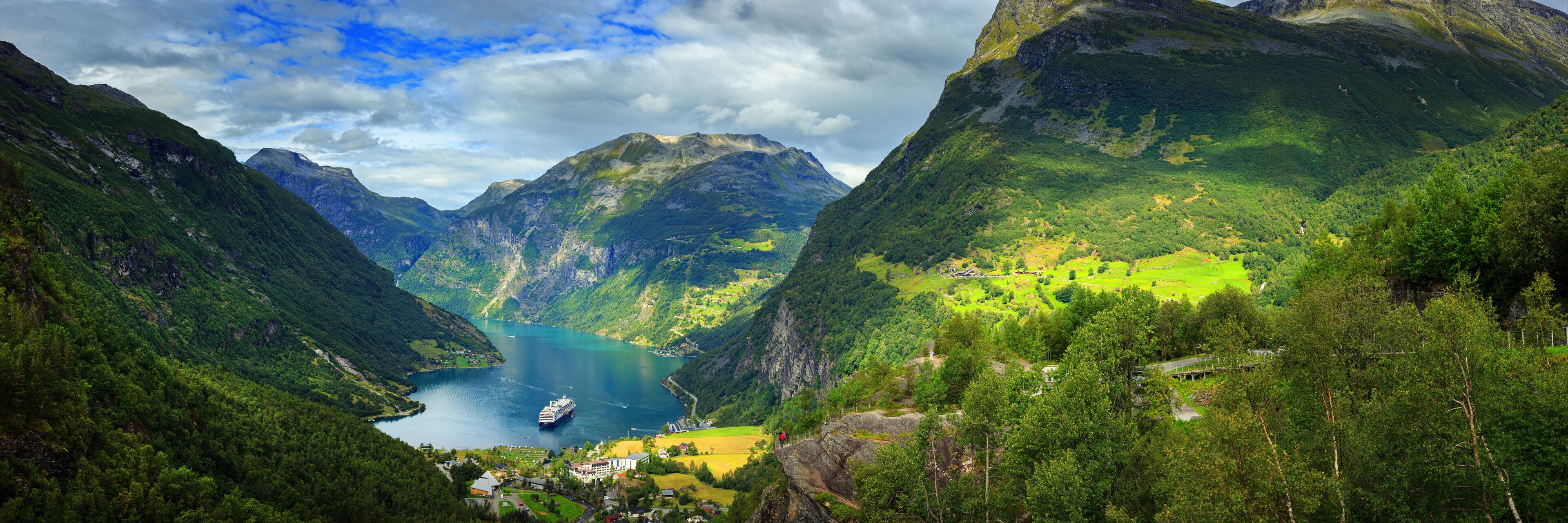 A fjord surrounded by mountains, a cruise ship, and a small village.