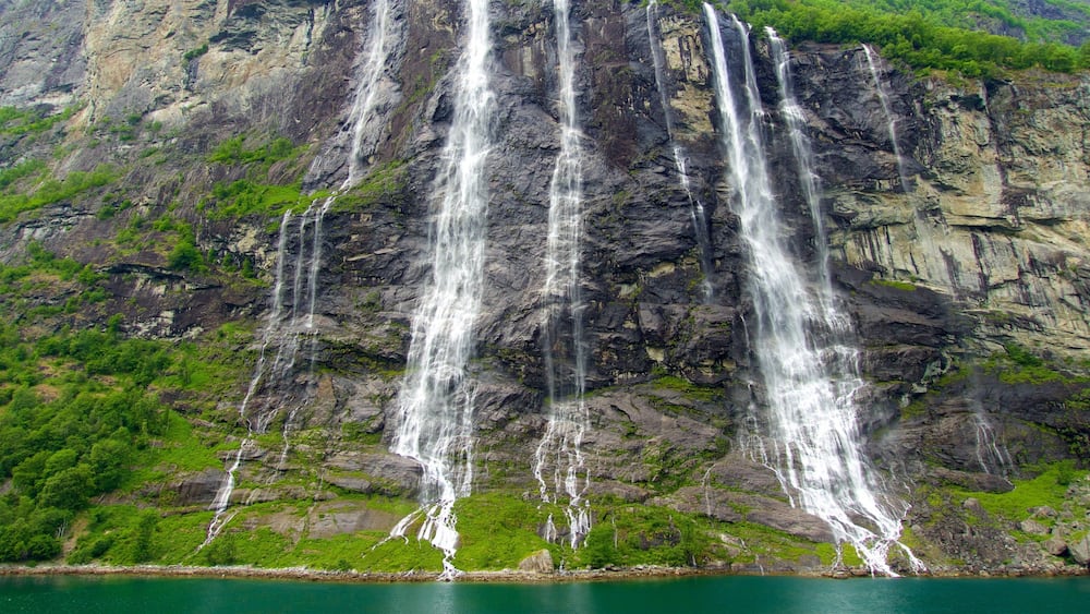 A multi-tiered waterfall cascading down a rocky cliff surrounded by lush greenery.