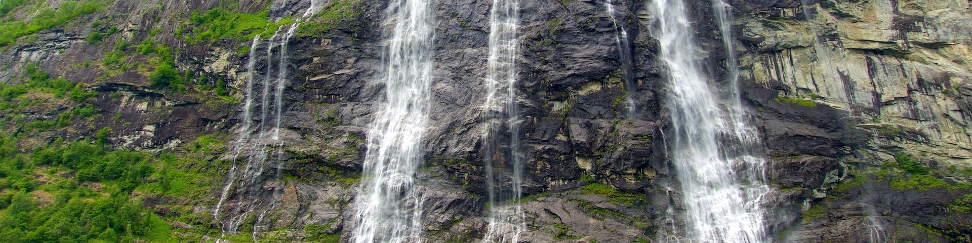Una cascada de varios niveles que se precipita por un acantilado rocoso, rodeada de abundante vegetación.
