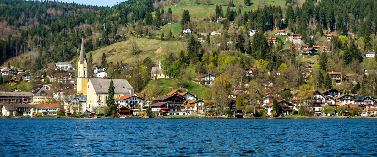 A lakeside village with houses, a church, and a hill with trees.