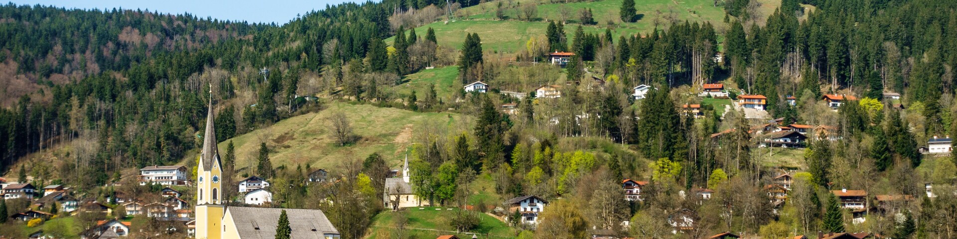 A lakeside village with houses, a church, and a hill with trees.
