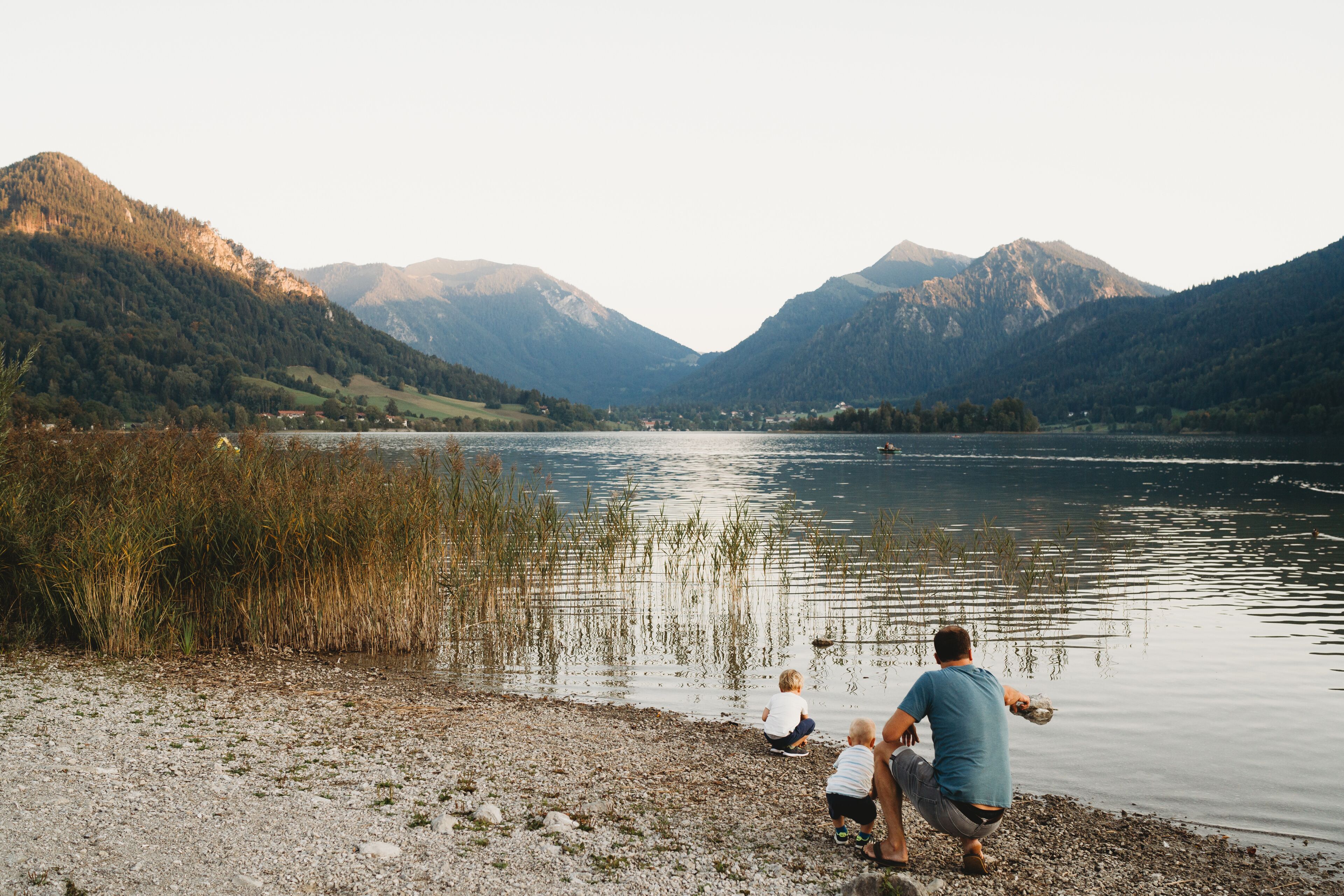 Un lago con montañas al fondo, una orilla rocosa y una persona con dos niños.