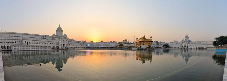 A serene lake with reflections of a grand white building and a golden temple during sunset.
