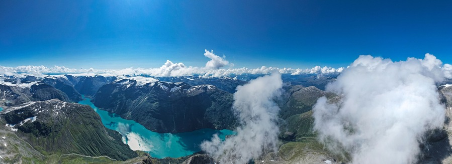 Un paisaje montañoso con un lago turquesa rodeado de picos nevados y nubes.