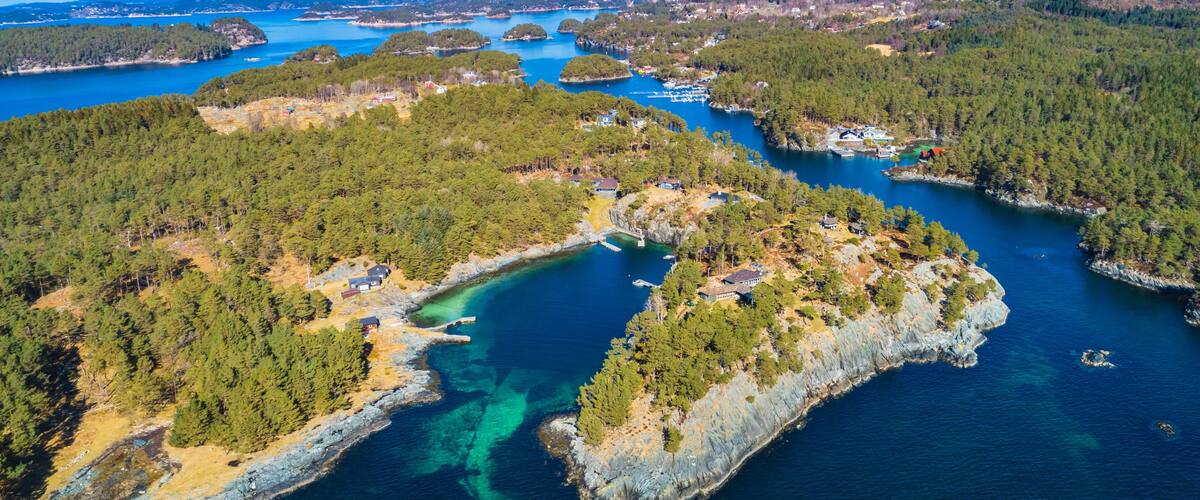 An aerial view of a coastal area with clear turquoise waters, surrounded by dense forests and rocky outcrops.