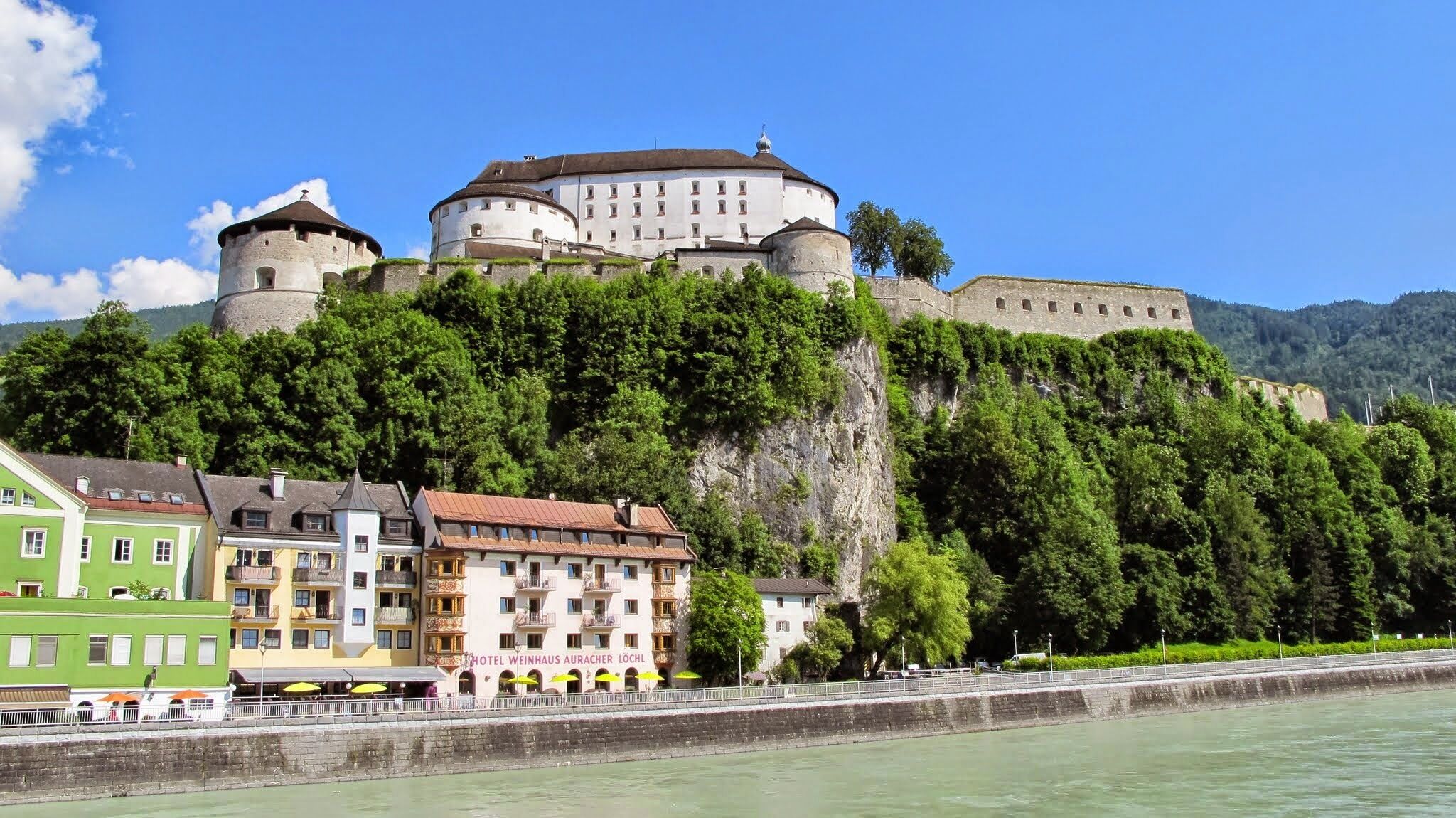 A historic castle on a hill with a river in the foreground.