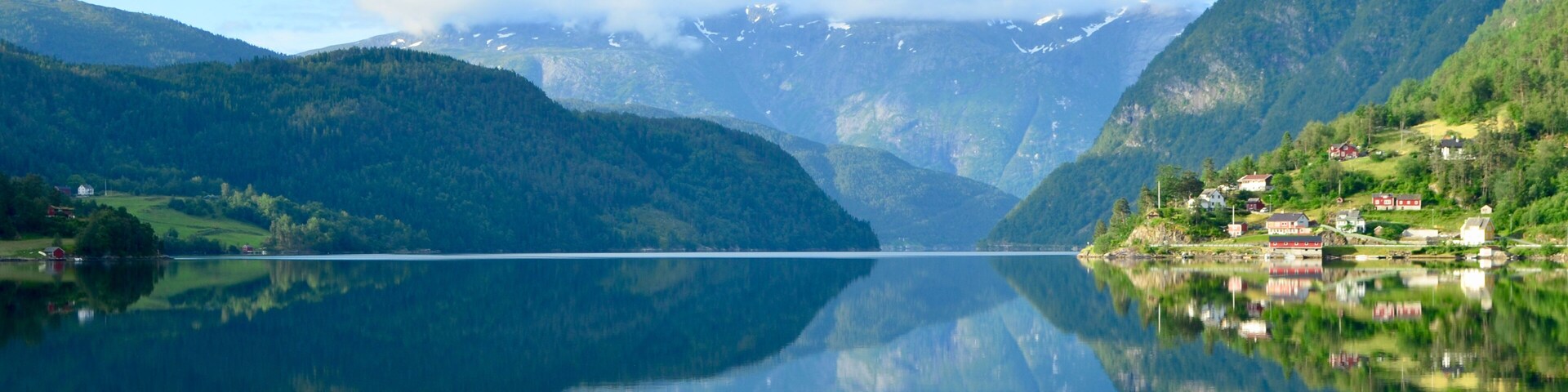 A calm lake with a clear reflection, surrounded by green hills and a few houses.