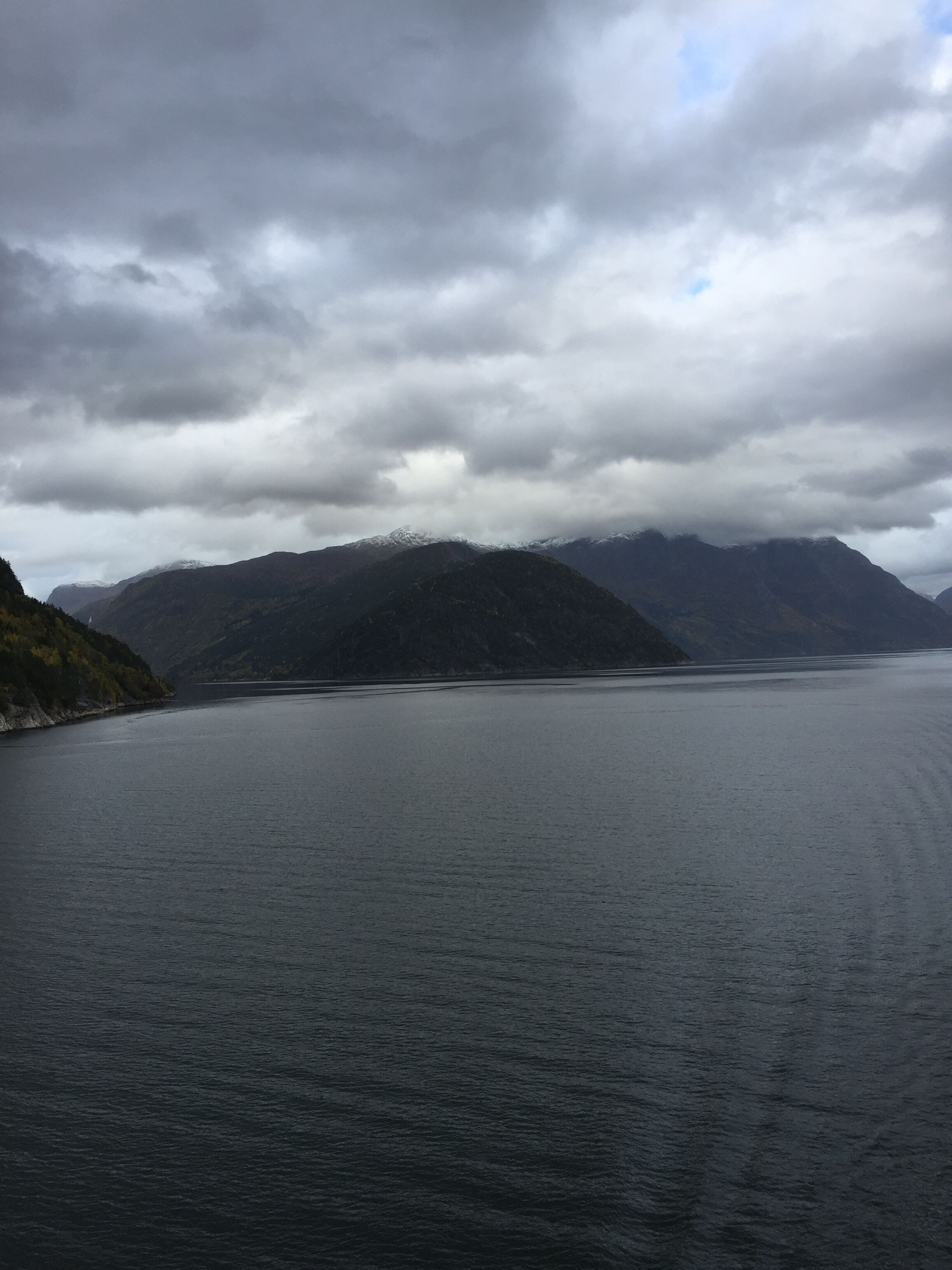 A calm lake surrounded by mountains under a cloudy sky.