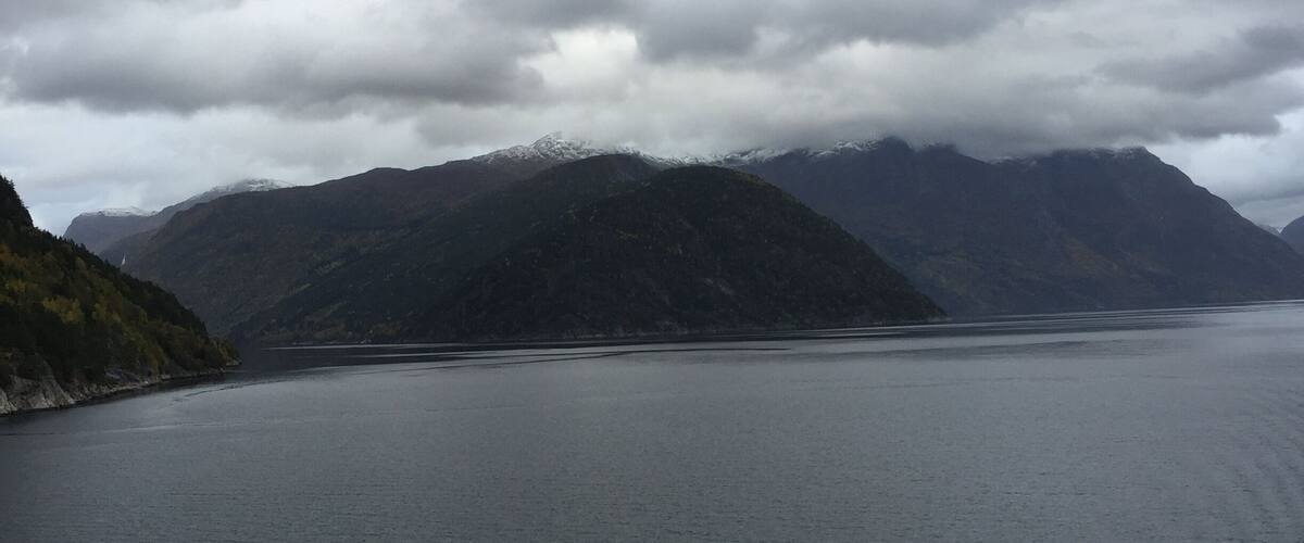 A calm lake surrounded by mountains under a cloudy sky.