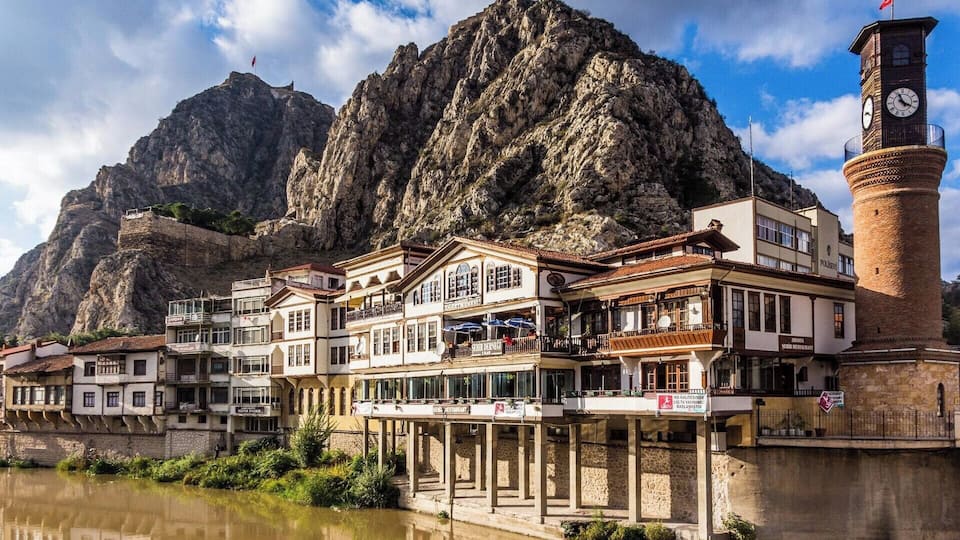 A riverside town with historic buildings, a clock tower, and a mountain backdrop.