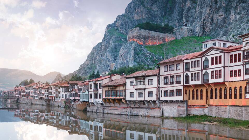 A river reflecting buildings, a stone bridge, and a mountainous backdrop.
