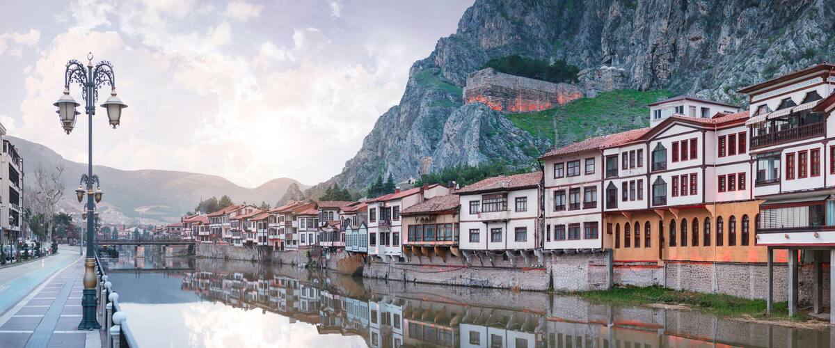 A river reflecting buildings, a stone bridge, and a mountainous backdrop.