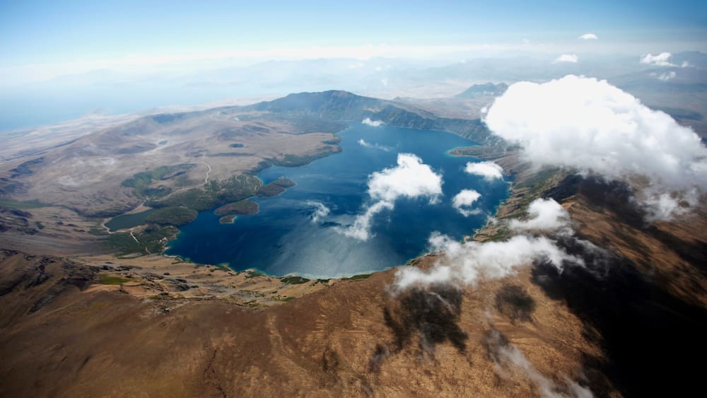 Un vaste paysage dominé par une étendue d’eau importante, entourée de montagnes et de nuages.