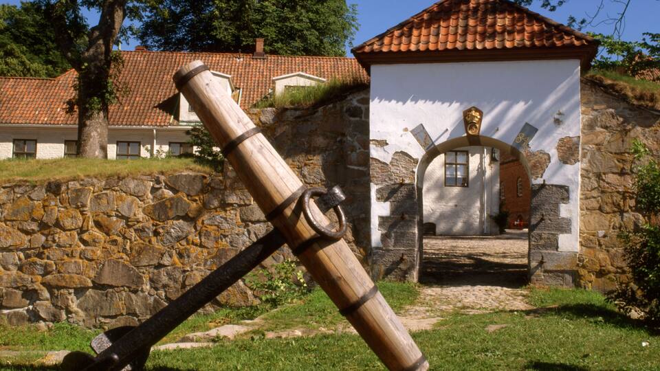 A stone wall, a wooden cannon, and a building with a tiled roof.