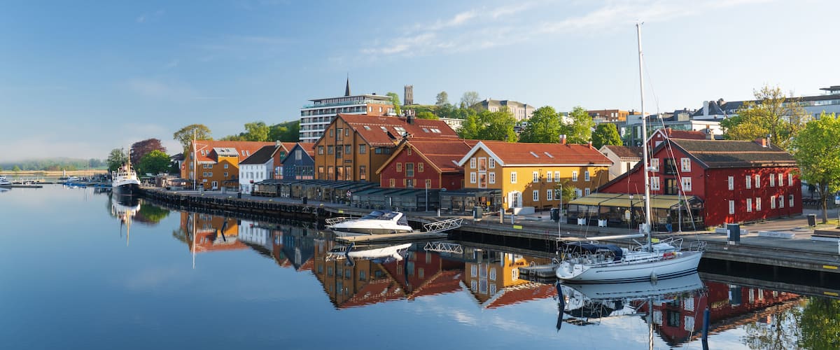 View of the historic waterfront with colorful wooden buildings and boats reflecting in the calm water of the harbor in Tonsberg, Vestfold, Norway.