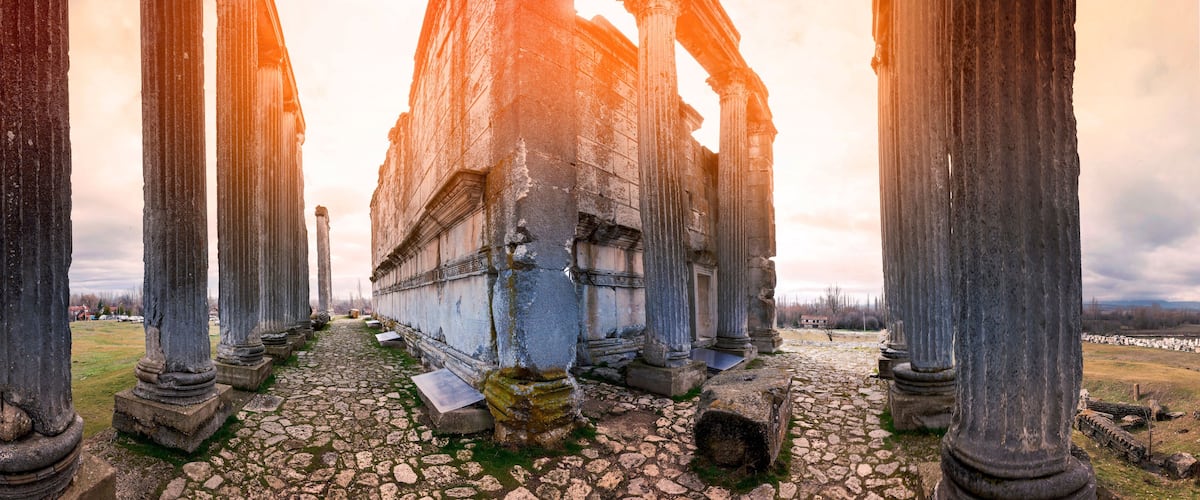Ancient stone columns and a ruined building with a cobblestone path.