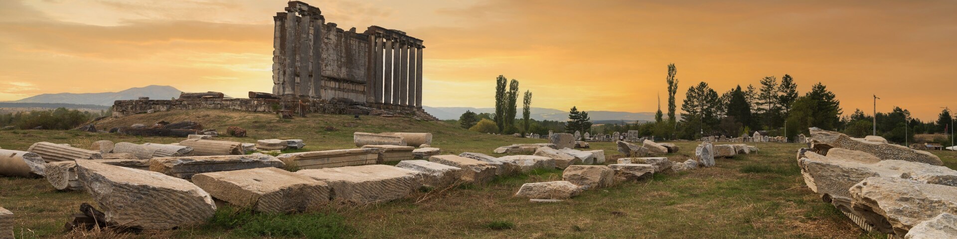 Ruinas antiguas con columnas y piedras dispersas, bajo un cielo al atardecer.