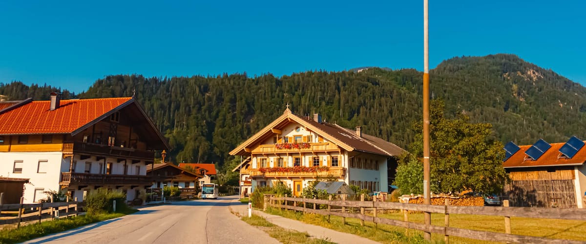 A mountain village with traditional wooden houses, a road, and a forested backdrop.