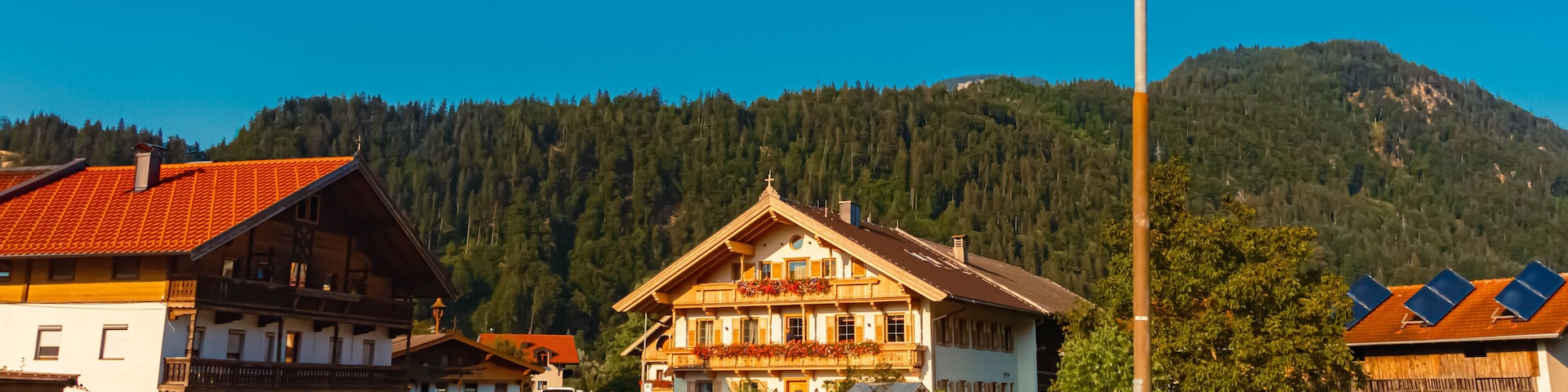 A mountain village with traditional wooden houses, a road, and a forested backdrop.