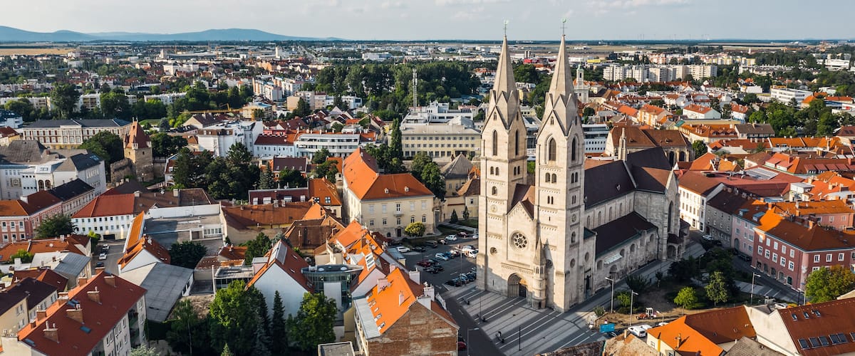 A cityscape with a prominent church featuring two tall spires and a large clock tower.