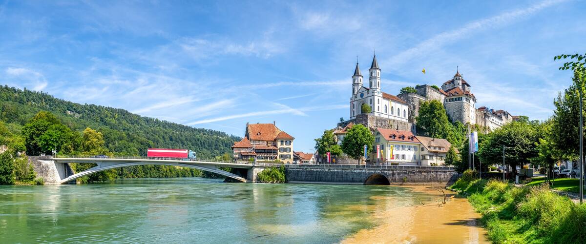 A river with a bridge, a red truck crossing, and historic buildings with towers.