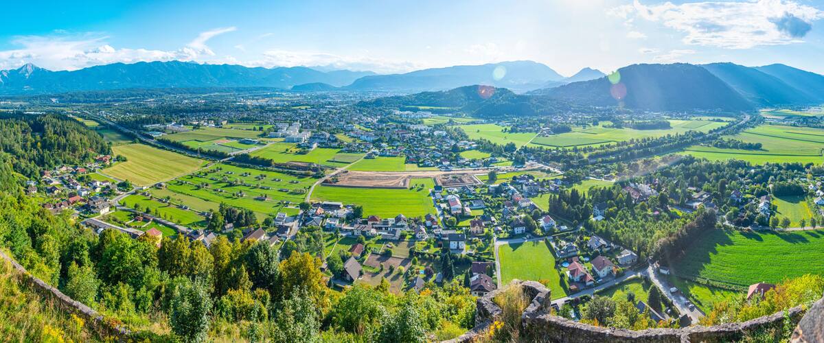 A panoramic view of a town nestled in a valley with surrounding mountains, green fields, and a river.