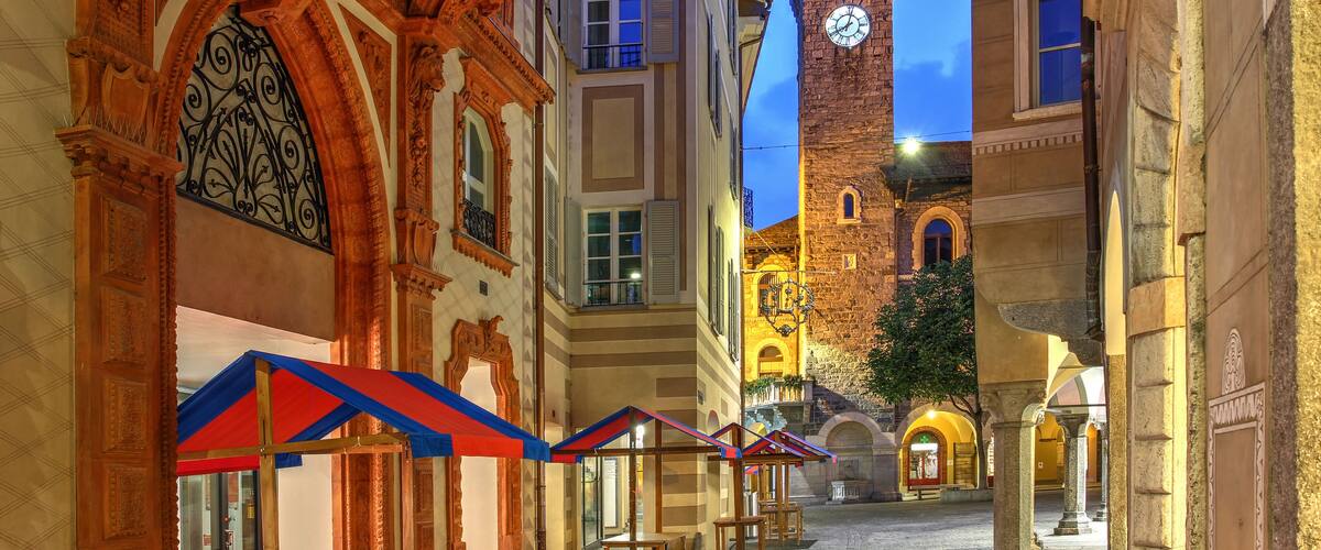 A historic European street with ornate architecture, a clock tower, and outdoor seating areas.