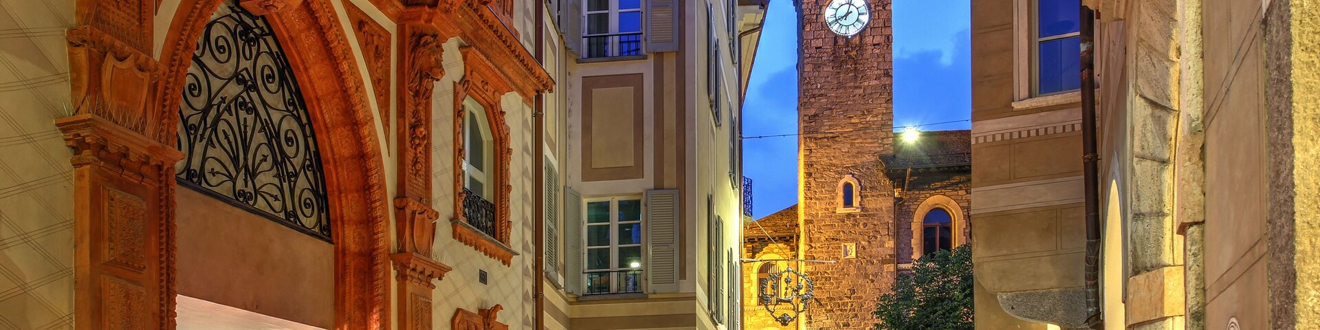 A historic European street with ornate architecture, a clock tower, and outdoor seating areas.