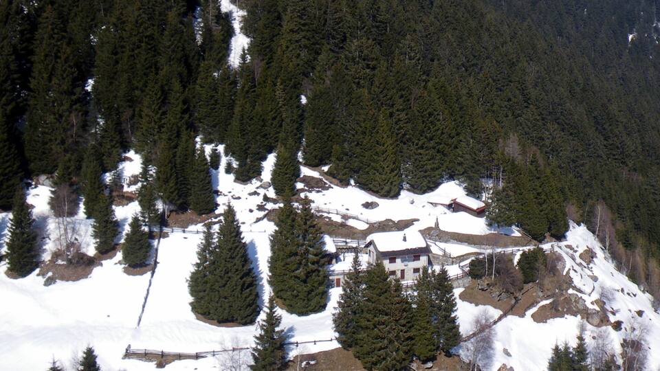 A snow-covered mountain with a small building surrounded by dense forest.