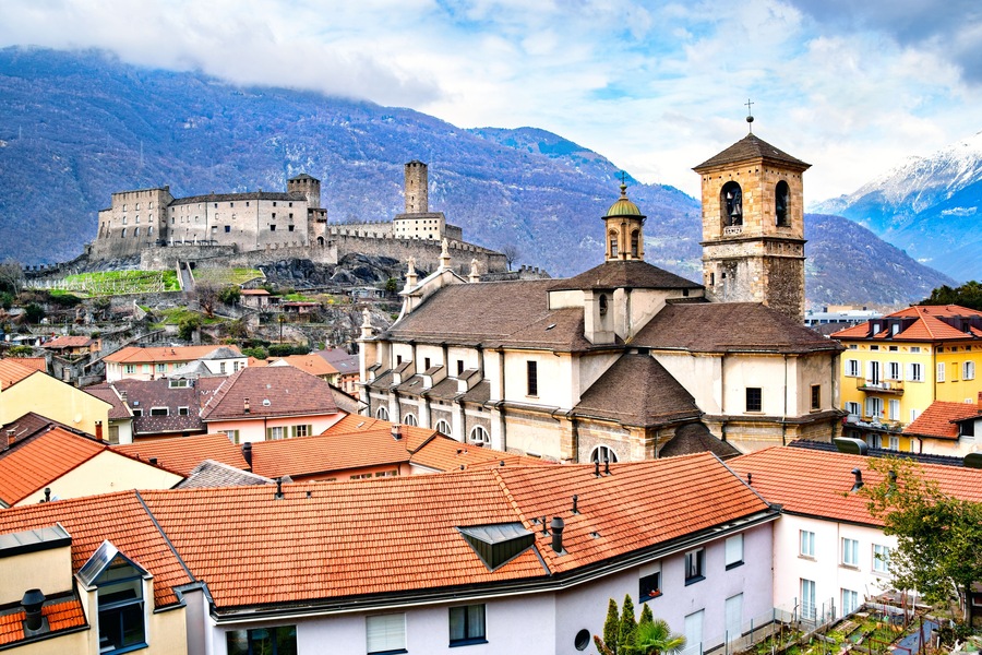 A historic town with a prominent castle on a hill, surrounded by mountains and colorful buildings.