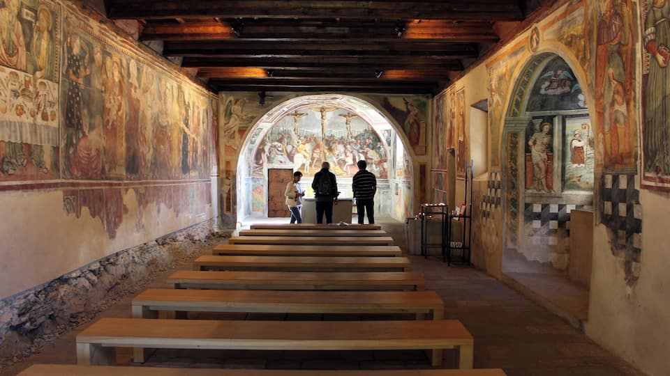 An interior with frescoes, wooden benches, and an arched window.