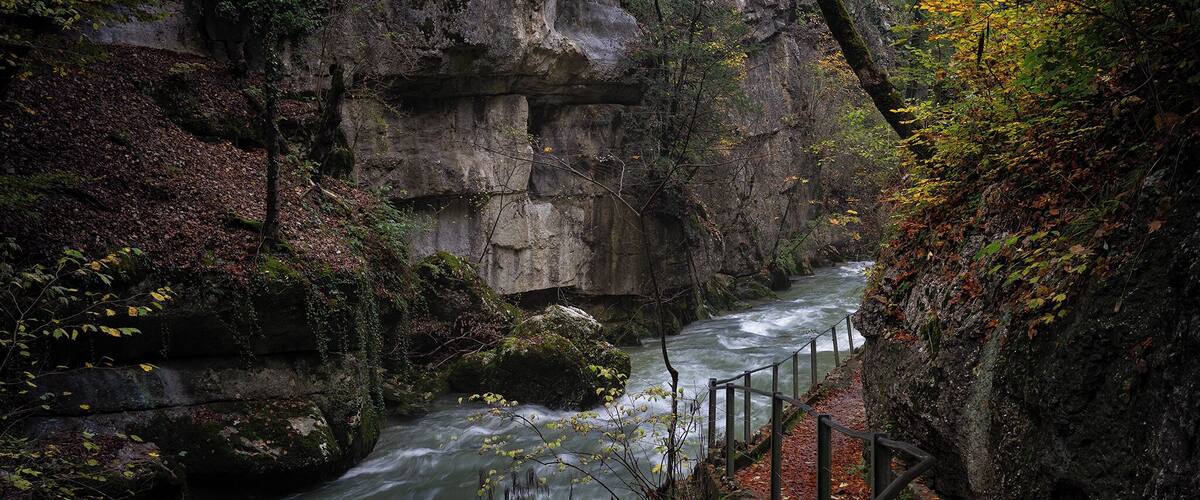 A river flowing through a rocky gorge with a wooden railing along the path.