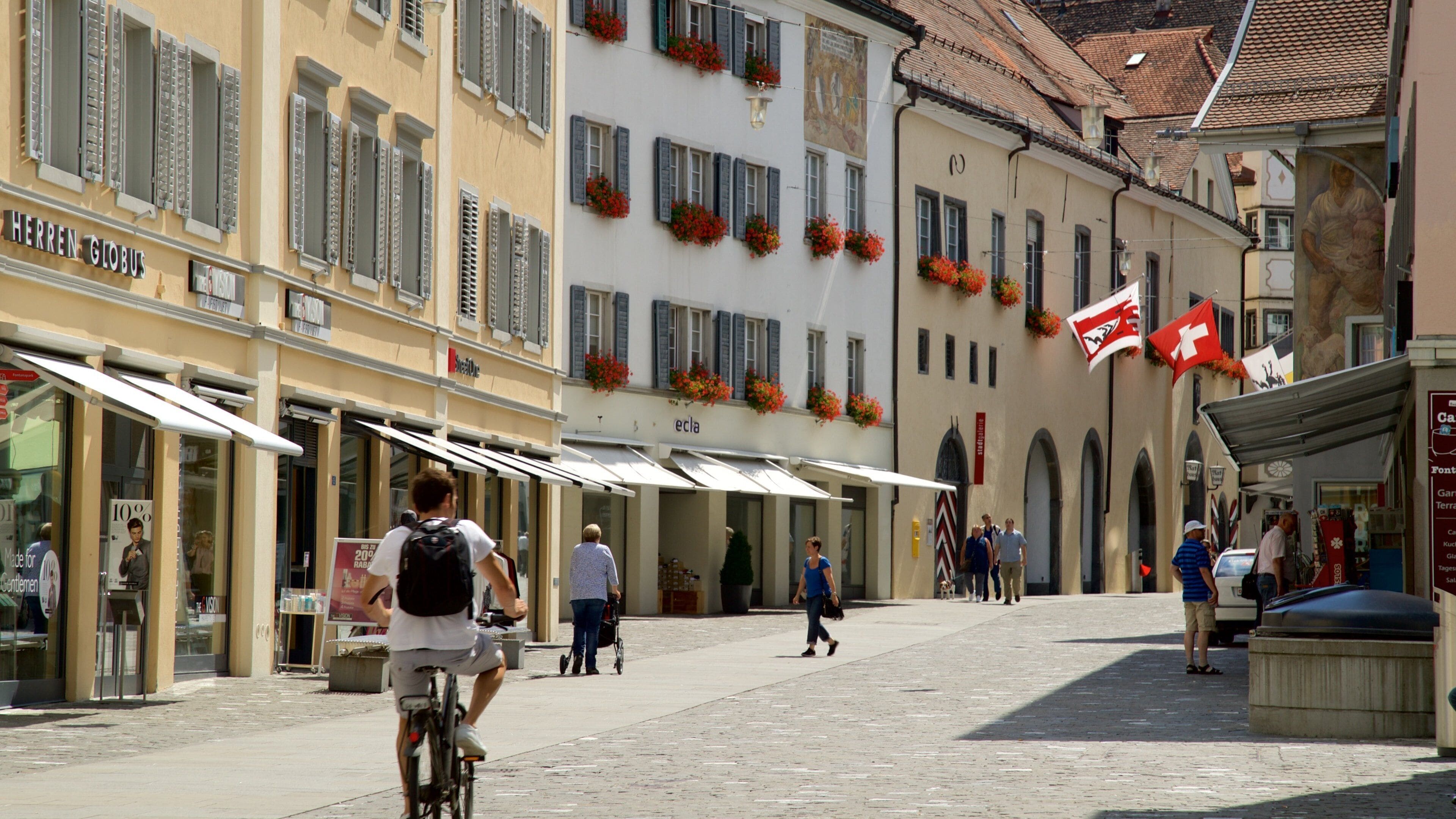 A cobblestone street lined with historic buildings, some with flower boxes and awnings.