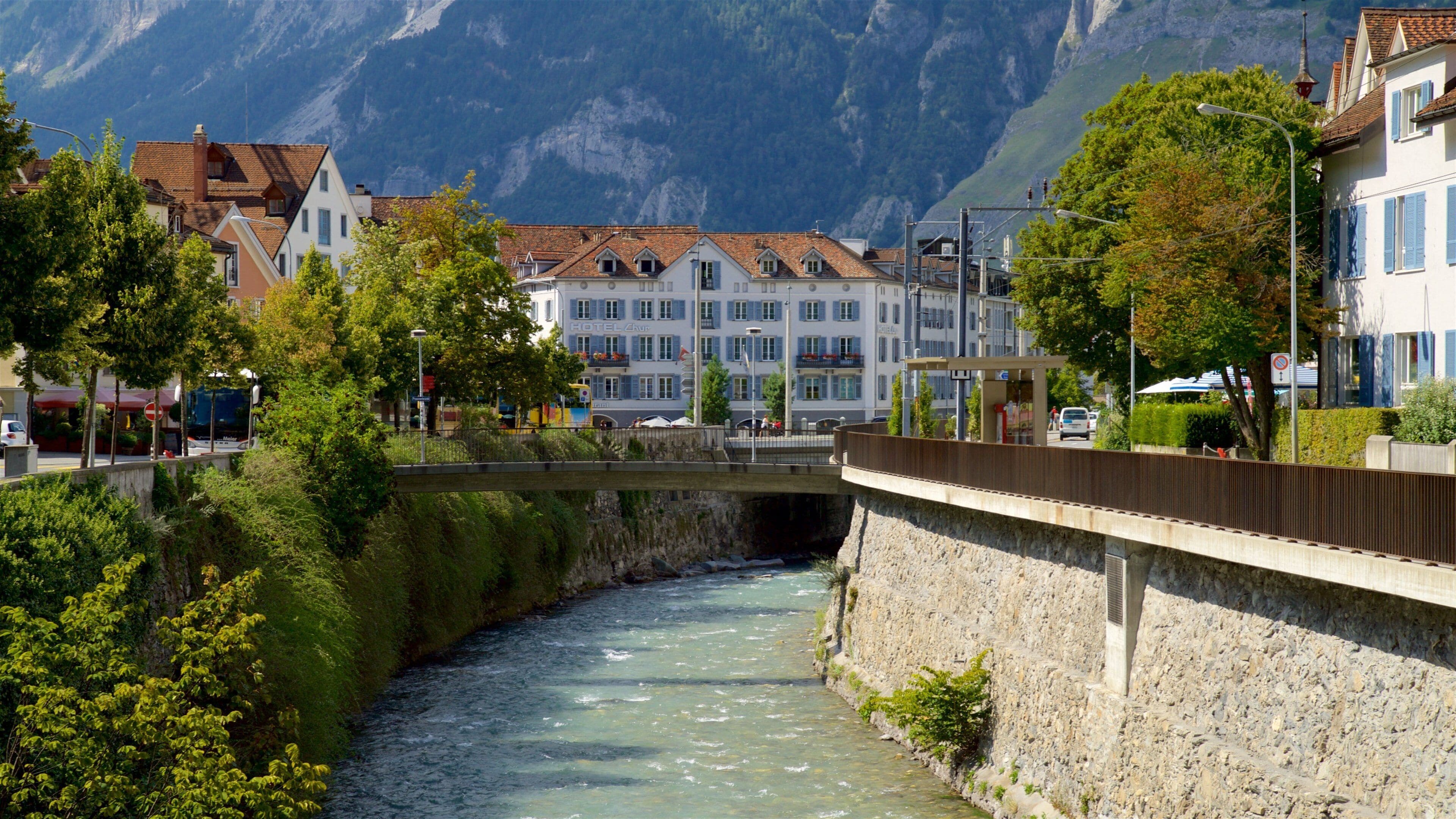 A river flowing under a bridge with buildings and mountains in the background.