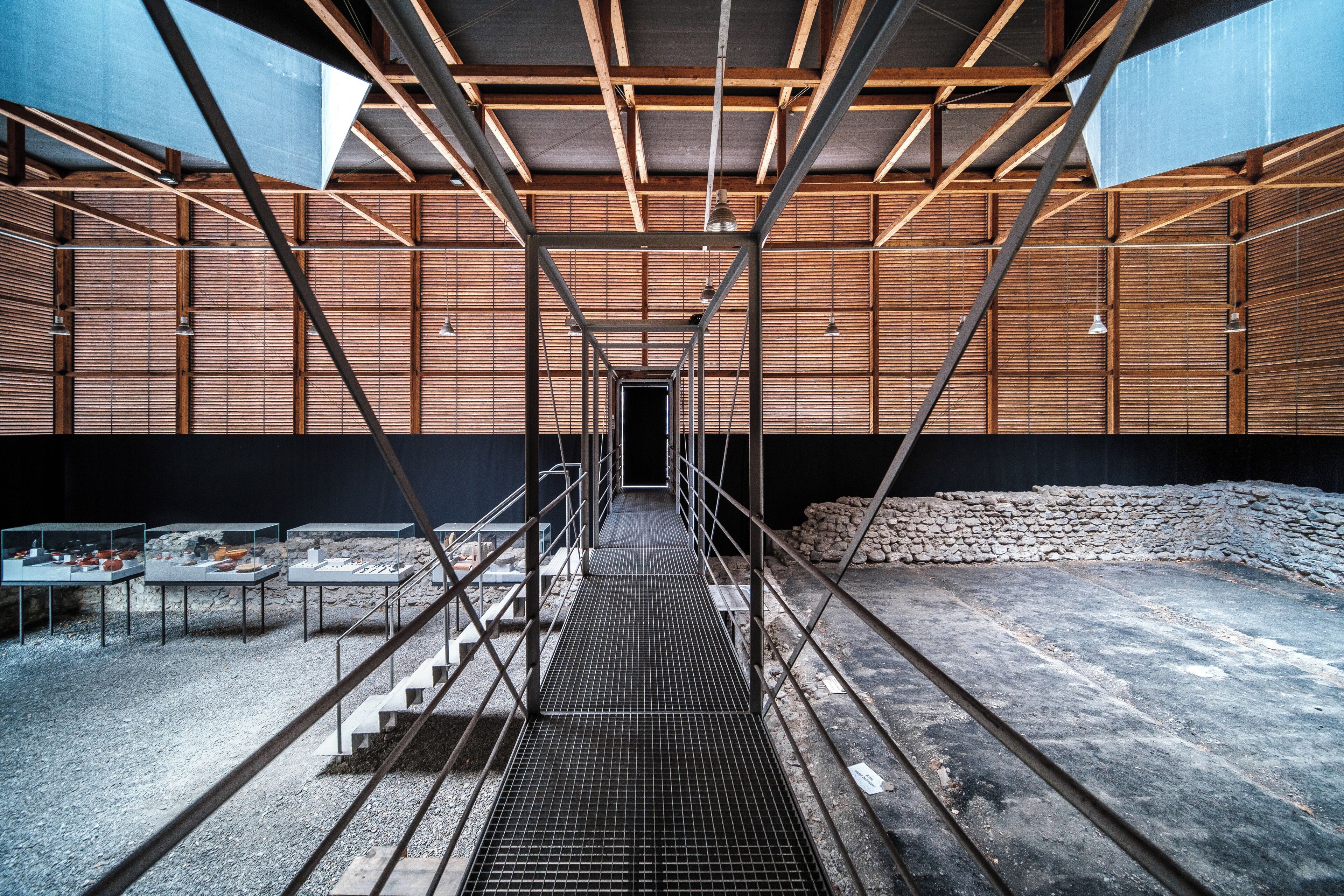 A modern architectural structure with a metal framework, wooden panels, and a central staircase leading to a dark doorway.