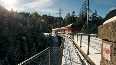 Un tren rojo sobre una vía cubierta de nieve, rodeado de árboles cargados de nieve y un cielo despejado.