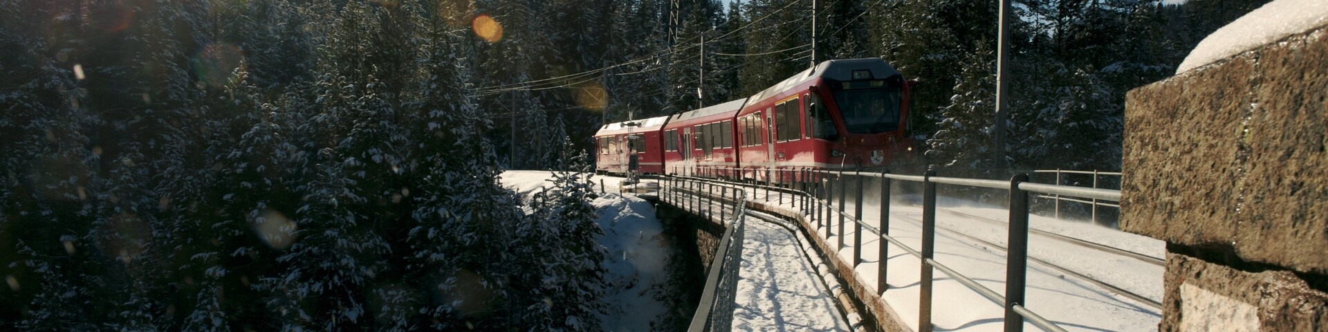 Un tren rojo sobre una vía cubierta de nieve, rodeado de árboles cargados de nieve y un cielo despejado.