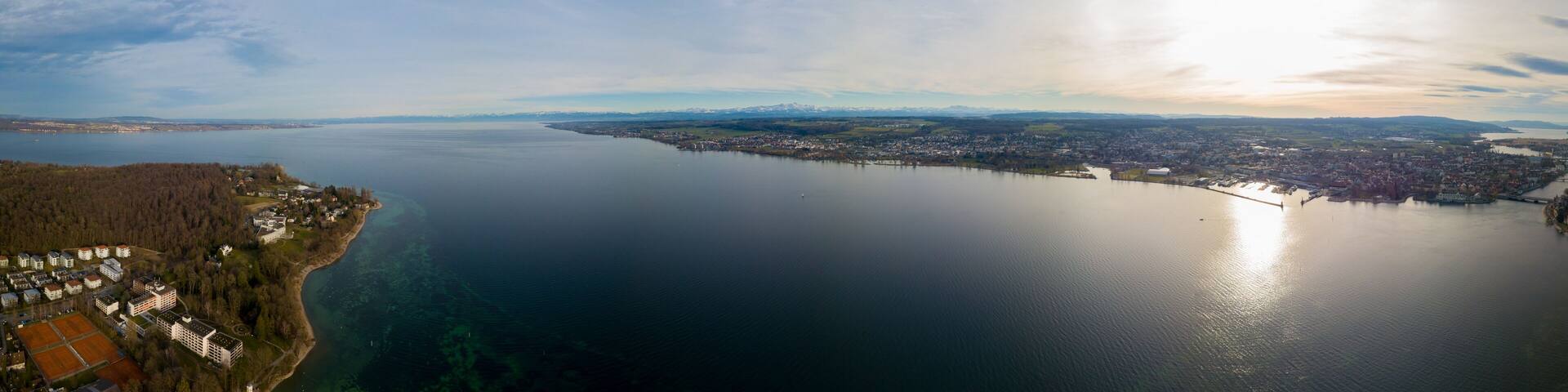A coastal city with a large body of water, a dense forested area, and a distant mountain range.