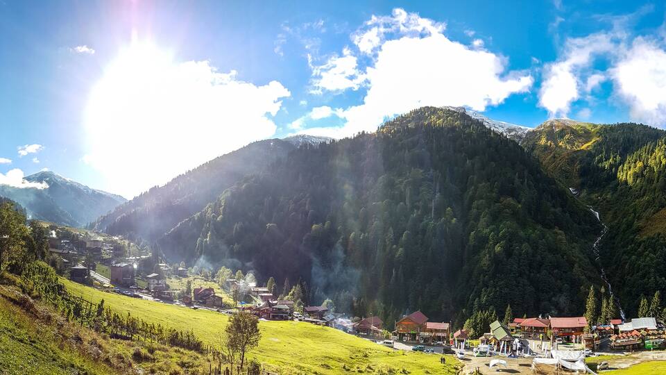 A mountain village with houses, a road, and a forested valley.