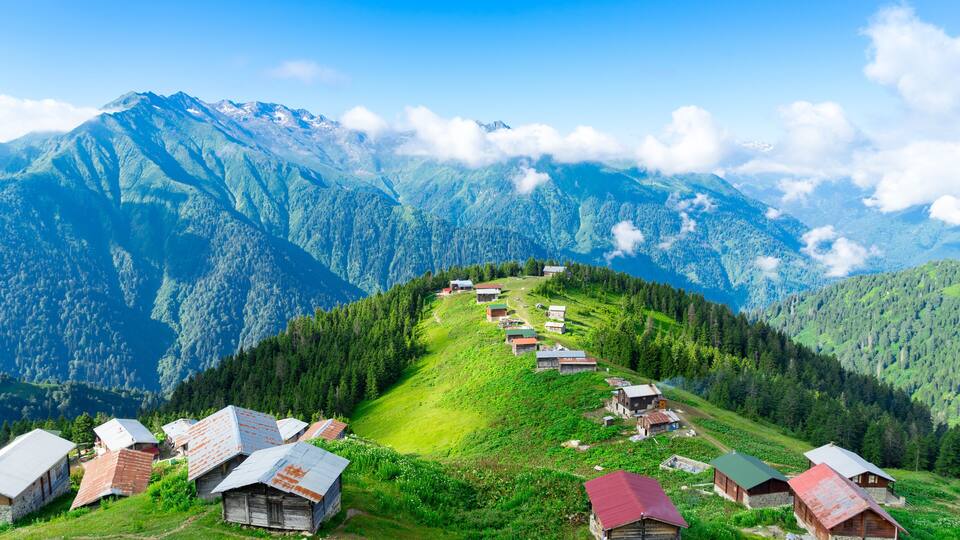 A village on a hillside with houses and a mountain range in the background.